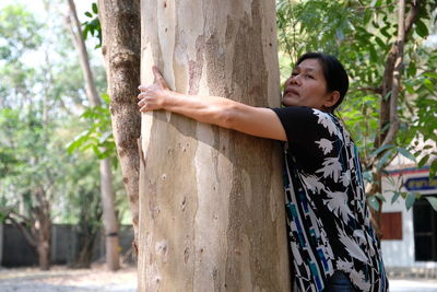 Side view of mature woman embracing tree trunk in forest