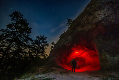 Silhouette man standing by illuminated cave at night