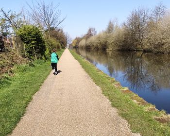 Rear view of boy riding push scooter on road by lake