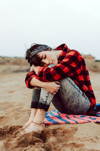 Thoughtful hipster woman sitting on sandy beach