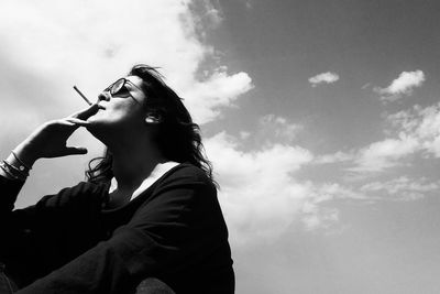 Low angle view of woman smoking cigarette while sitting against sky