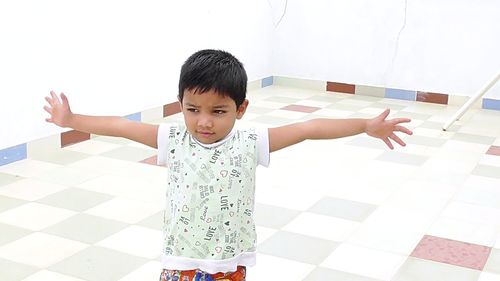 Cute boy with arms outstretched looking away while standing on floor at home