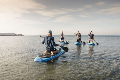 Male instructor teaching paddleboarding to man and women in sea during vacation