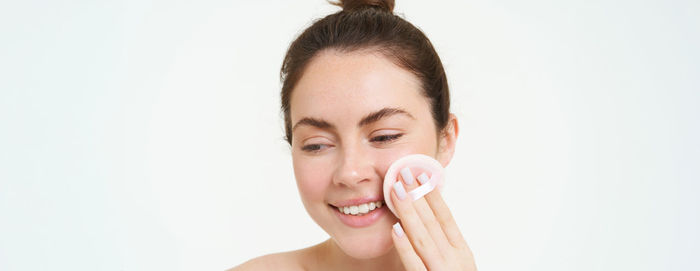 Portrait of smiling young woman applying make-up against white background