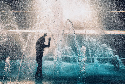 Man standing amidst water splashing in fountain
