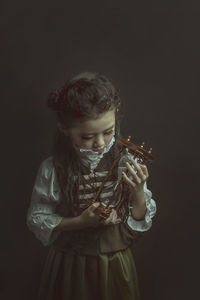 Girl wearing costume while holding hourglass against black background