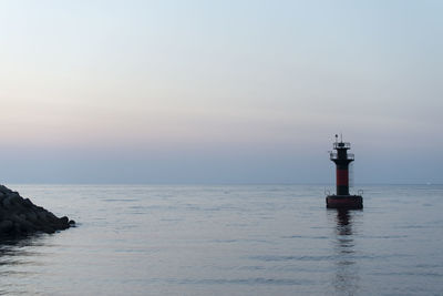 Lighthouse on sea against sky during sunset