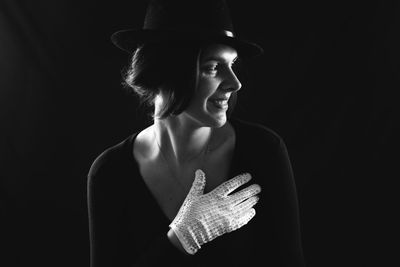 Smiling young woman wearing glove and hat against black background