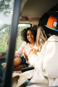 Through window of cheerful young asian woman sitting on driver seat of camper vehicle while traveling with girlfriend through nature