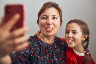 Mother with her little daughter showing tongue making video call using mobile phone