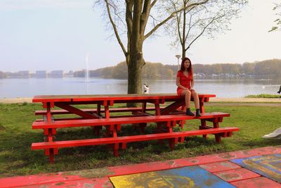 Woman sitting on bench by lake against sky