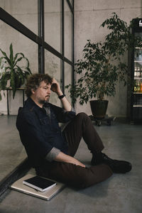 Side view of depressed professional businessman leaning on glass wall at office