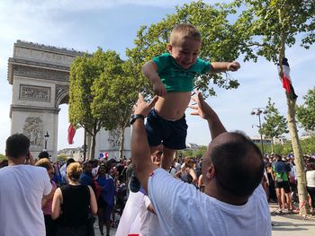 Playful father throwing son in air on crowded city street