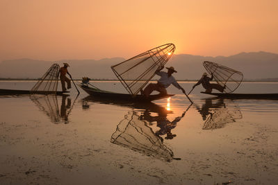 Fishermen fishing in lake against sky during sunset