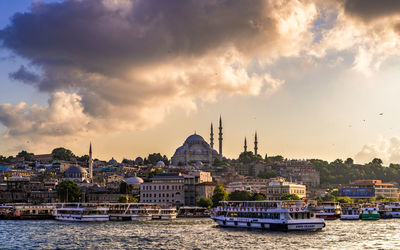 View of buildings by river against cloudy sky