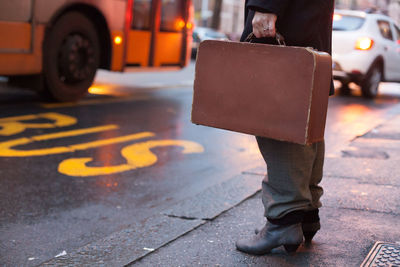 Low section of businessman carrying suitcase while standing on city street