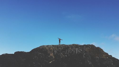 Low angle view of woman standing on rock formation against blue sky