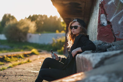 Young woman sitting in sunglasses against sky during sunset