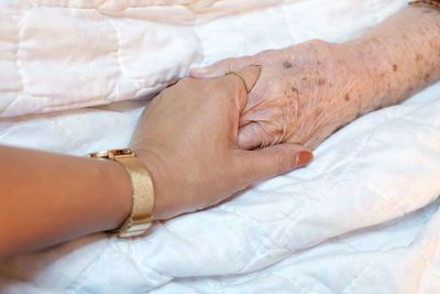 Cropped woman holding mother hand on bed