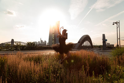 Woman dancing on field in city against sky during sunset