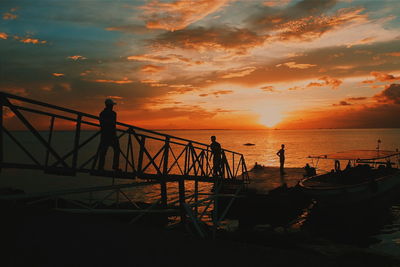 Silhouette people at sea against sky during sunset