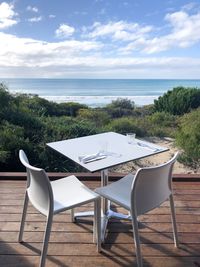 Empty chairs and table by sea against sky