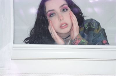 Portrait of young woman looking through window at home