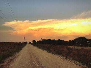 Road amidst field against sky during sunset