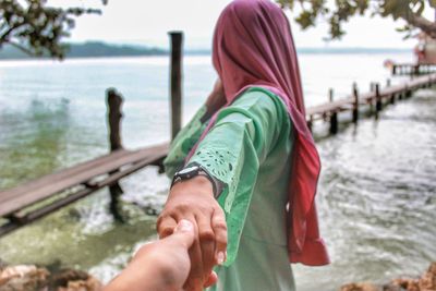 Cropped image of man holding woman hand by lake