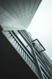 Low angle view of man peeking through window from building against clear sky