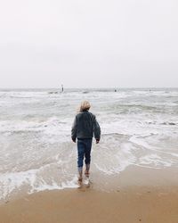 Rear view of boy on beach against sky