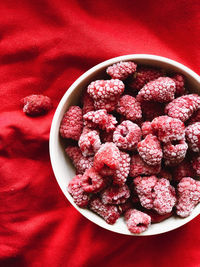 Frozen raspberries in a white ceramic plate stands on a red background