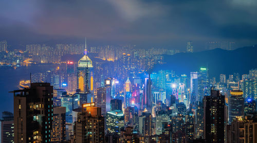 Illuminated buildings in city against cloudy sky