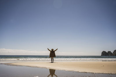 Woman standing with arms raised at shore on sunny day