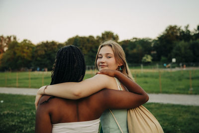 Portrait of smiling teenage girl with arm around friend walking at park