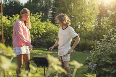 Teenage siblings grilling in back yard on sunny day