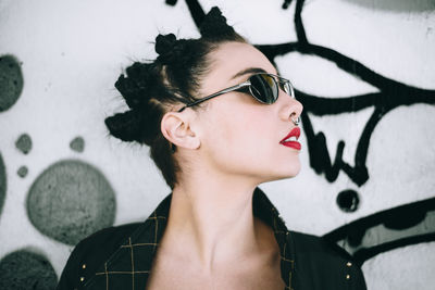 Close-up of young woman standing by graffiti wall