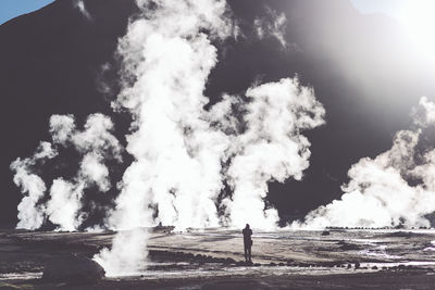 Rear view of man standing by waterfall against sky