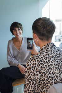 Young woman taking photo of smiling friend while sitting at restaurant