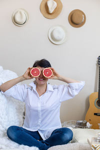 Woman holding grapefruit while sitting on bed at home