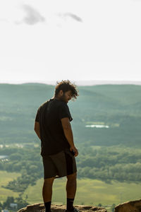 Rear view of young man standing on rock against mountains