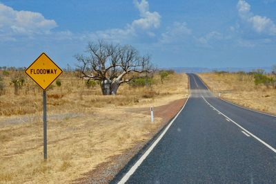 Road sign by bare trees against sky