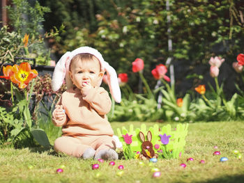 Little cute caucasian baby girl in a bunny ears headband sits on a lawn 