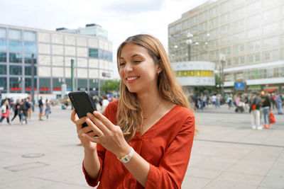 Smiling woman using smartphone in alexanderplatz square in berlin, germany