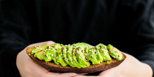 Female hand holding healthy avocado toast. ripe hass avocado, wholegrain bread, sesame flax seeds.