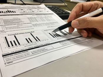 Cropped hand of person holding pen while writing on document at table