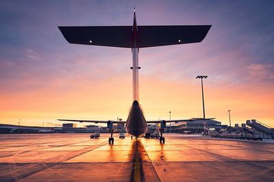 Airplane on airport runway against sky during sunset