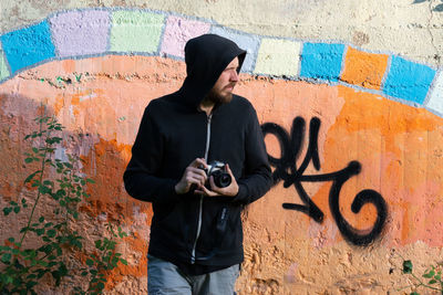 Full length of man photographing against graffiti wall