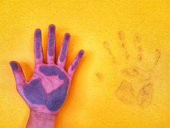 Cropped image of hand with paint on yellow wall