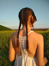 Rear view of young woman with braided hair standing on field against sky